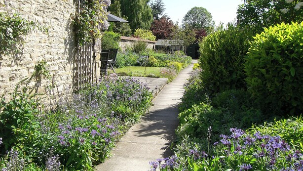 A garden pathway with stone walls and flowering plants. - Eden House Holiday Cottage (Pickering)