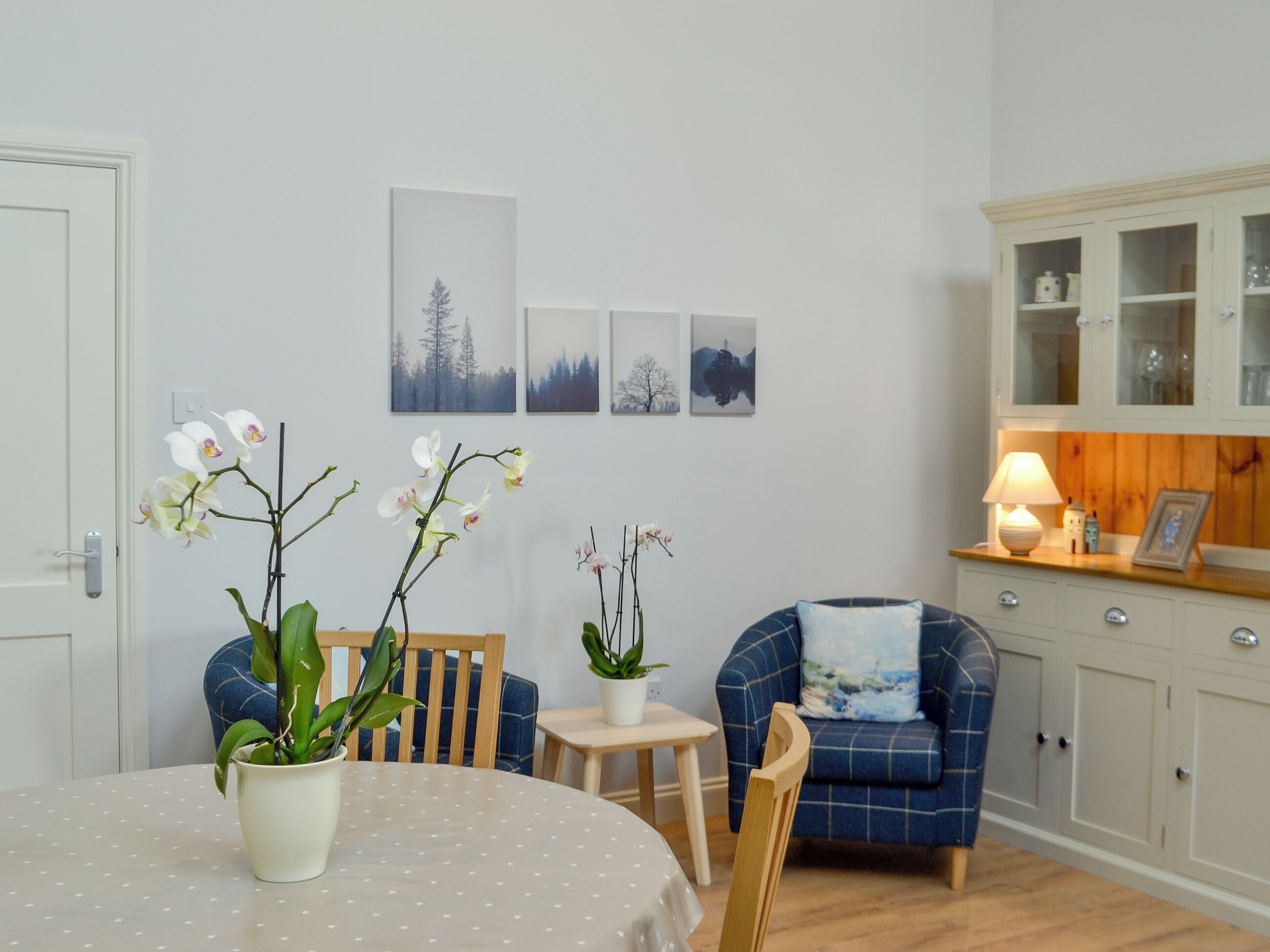 A dining area with a round table, chairs, potted plants, and wall art.