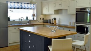 A kitchen with a central island, white cabinets, a built-in oven, and a window with a blue and white valance.