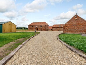 A gravel driveway leading to a farmstead with barns and a green field.