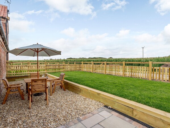 A patio with a table and chairs, a wooden fence, and a grassy area.