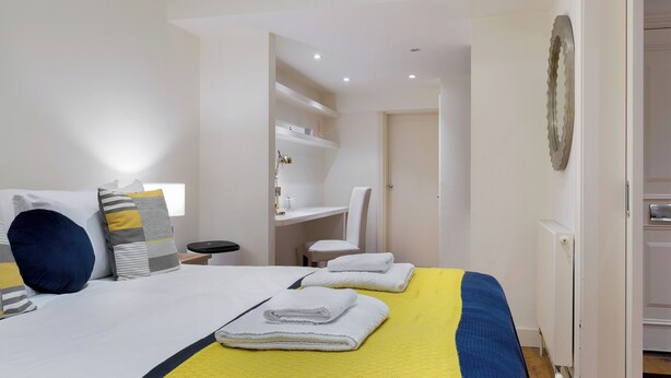 Une chambre d’hôtel avec un lit, un bureau et une chaise. Il y a des serviettes sur le lit et un radiateur au mur.