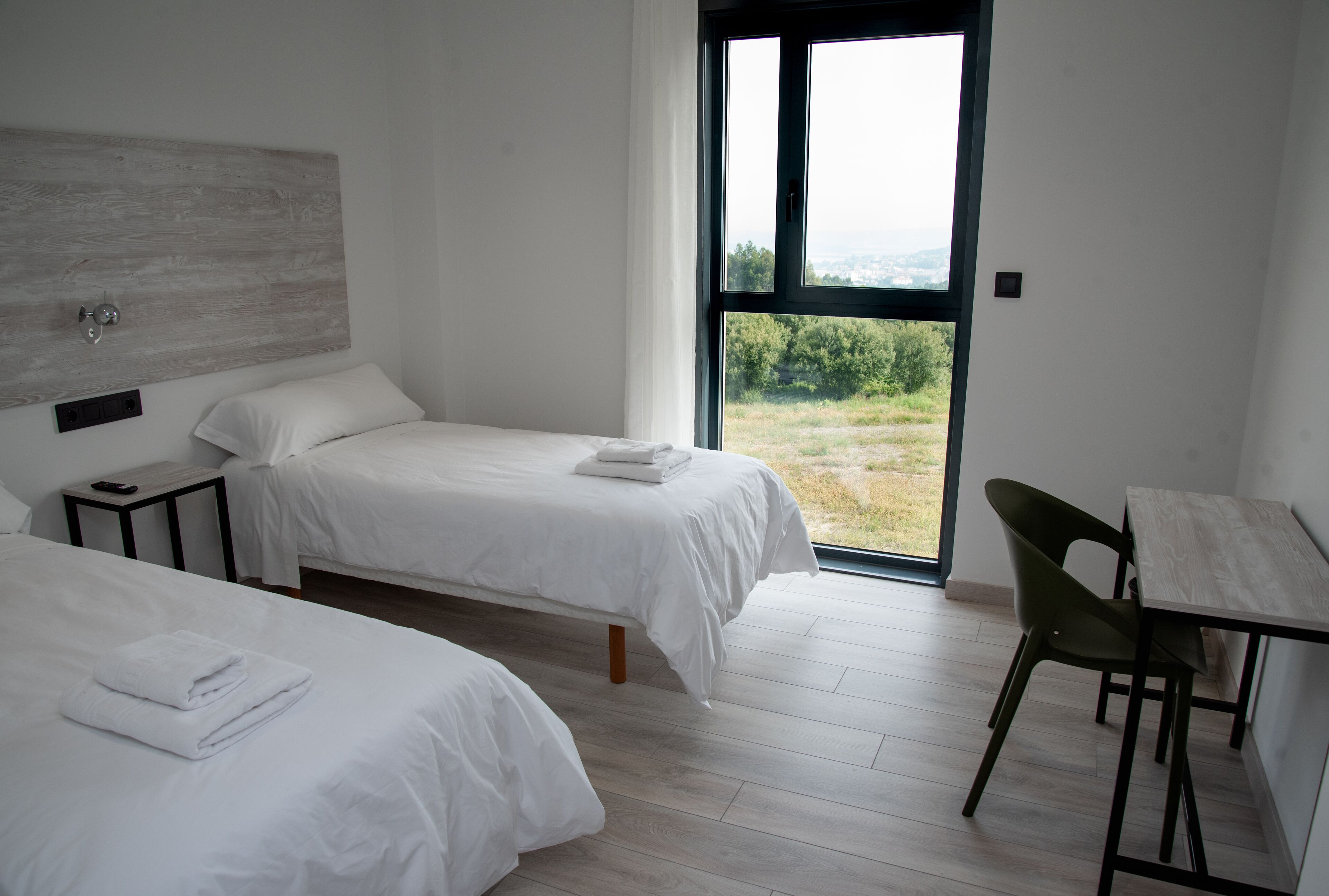 A hotel room with two beds, a small table, and a view of the outdoors.