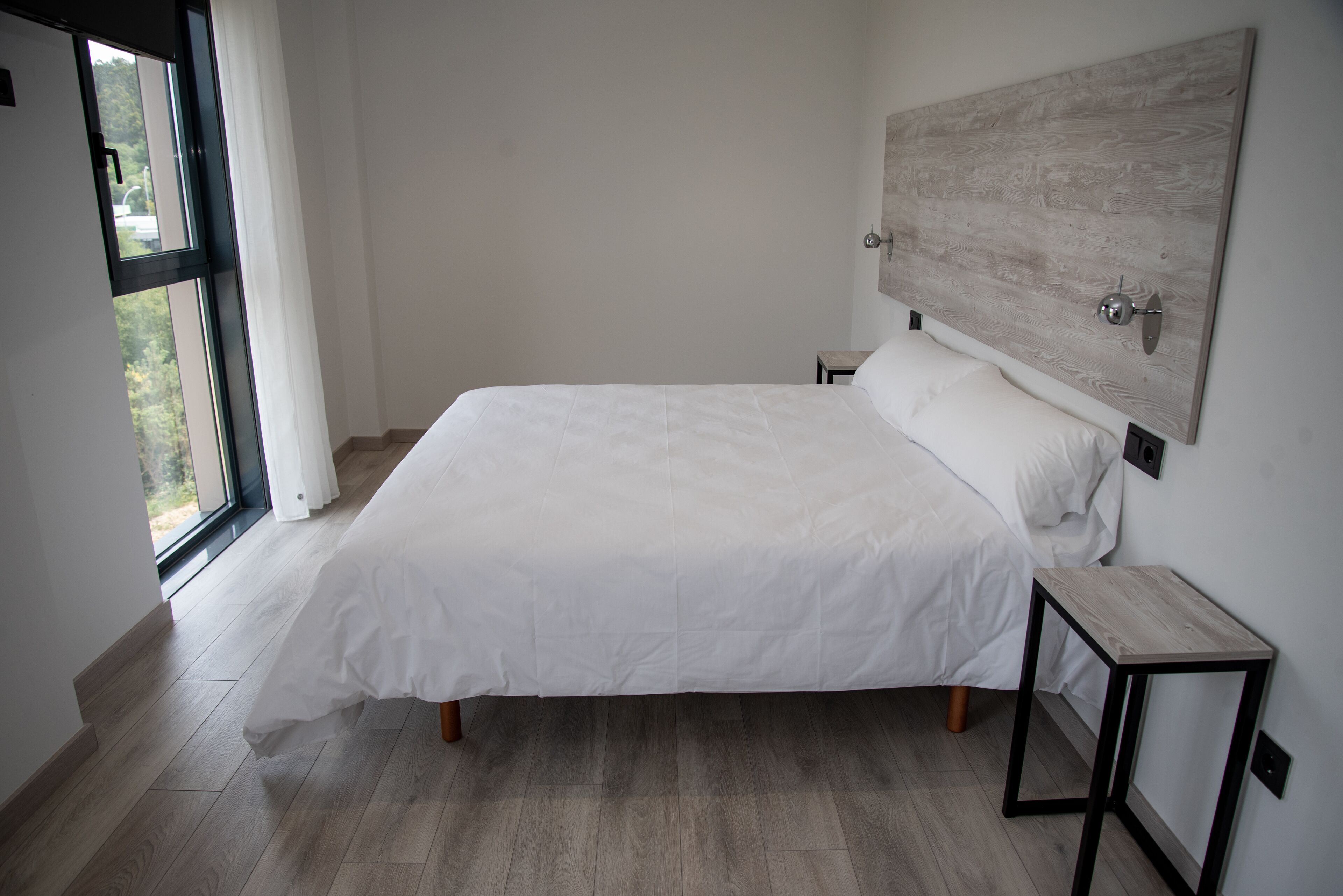 Un dormitorio con una cama grande, una mesita de noche, un cabecero de madera y una ventana con cortinas.