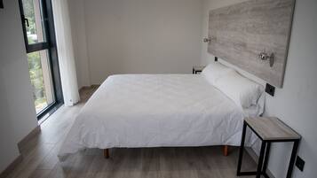 Un dormitorio con una cama grande, una mesita de noche, un cabecero de madera y una ventana con cortinas.
