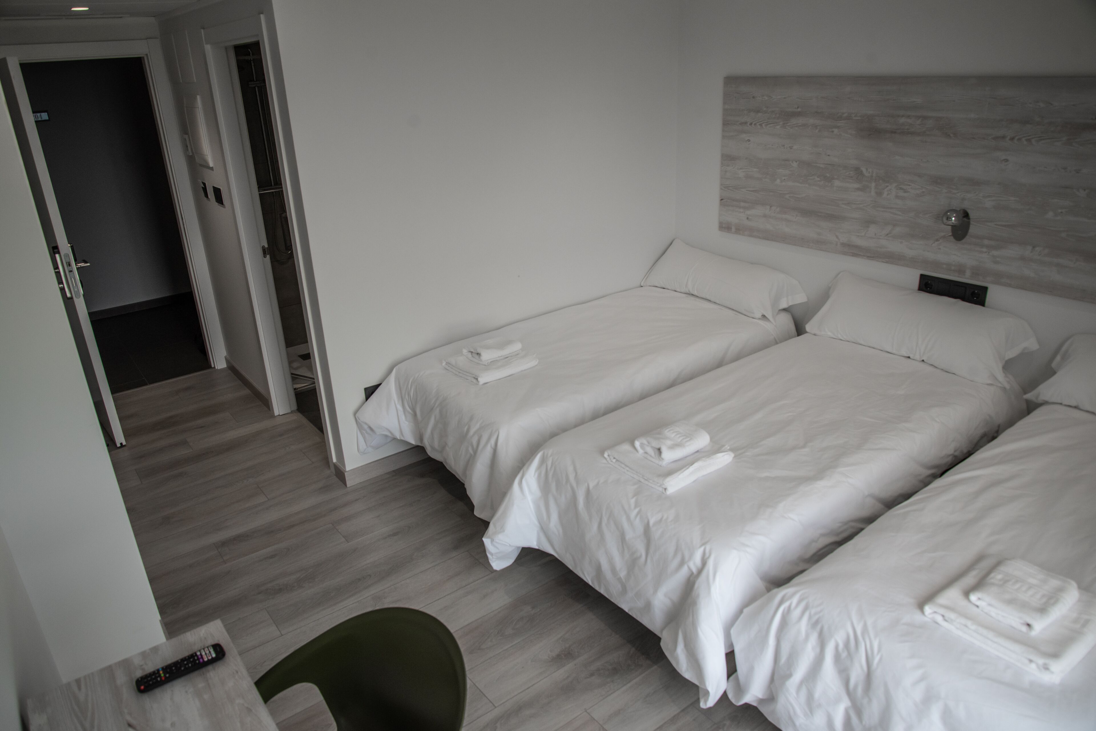 A hotel room with two beds, a green chair, and a remote control on a table.