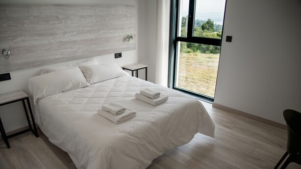 Een moderne slaapkamer met een groot bed, een nachtkastje en uitzicht op een grasveld door een groot raam.