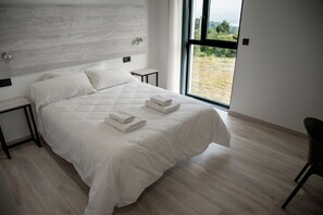 A modern bedroom with a large bed, a nightstand, and a view of a grassy field through a large window. - Hotel Chips Fene (Fene)