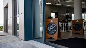 Een moderne hotelentree met een glazen deur, een bord met 'Hotel Chips Abierto' erop en een zithoek met witte stoelen en een houten balie.