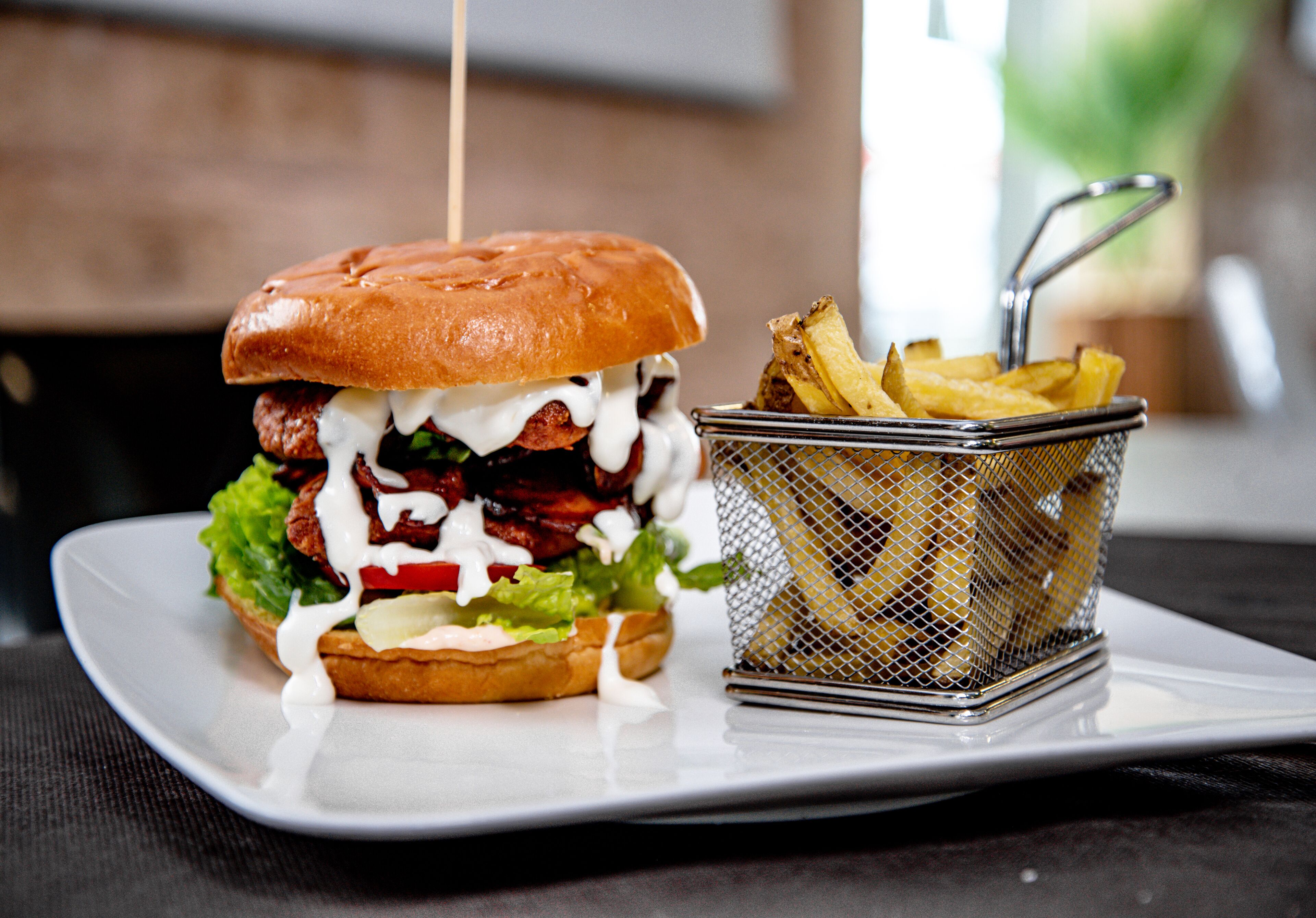 Ein Burger mit Zahnstocher, Salat, roter Tomate und Pommes auf einem weißen Teller.