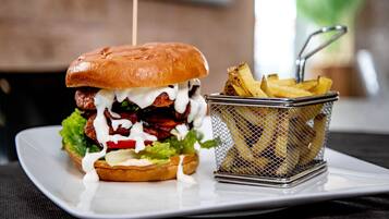 Ein Burger mit Zahnstocher, Salat, roter Tomate und Pommes auf einem weißen Teller.