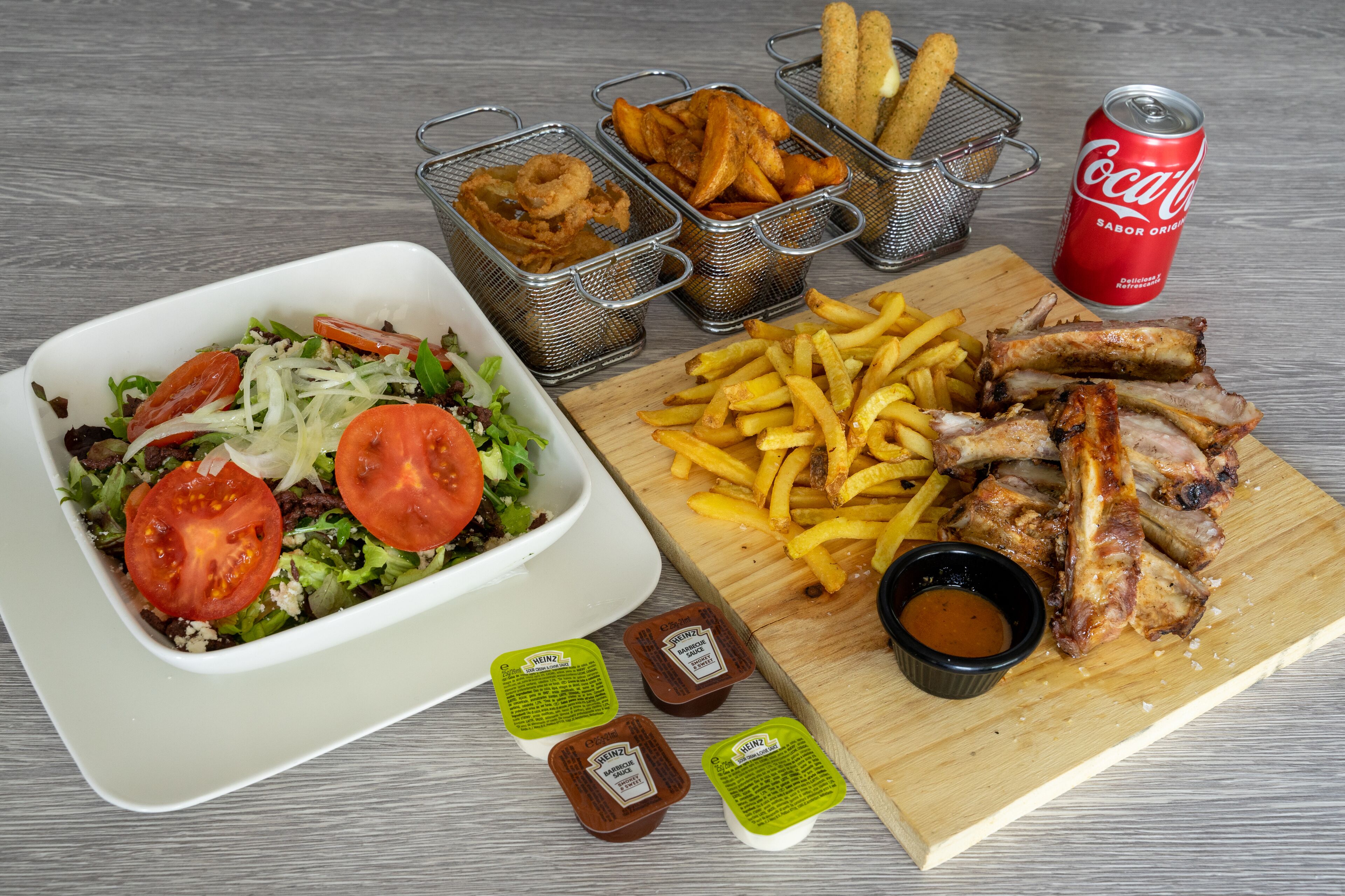 A meal consisting of a salad, fries, ribs, and a soda can.