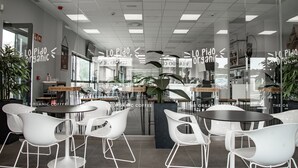Een modern café interieur met witte stoelen, tafels en een plant in het midden.