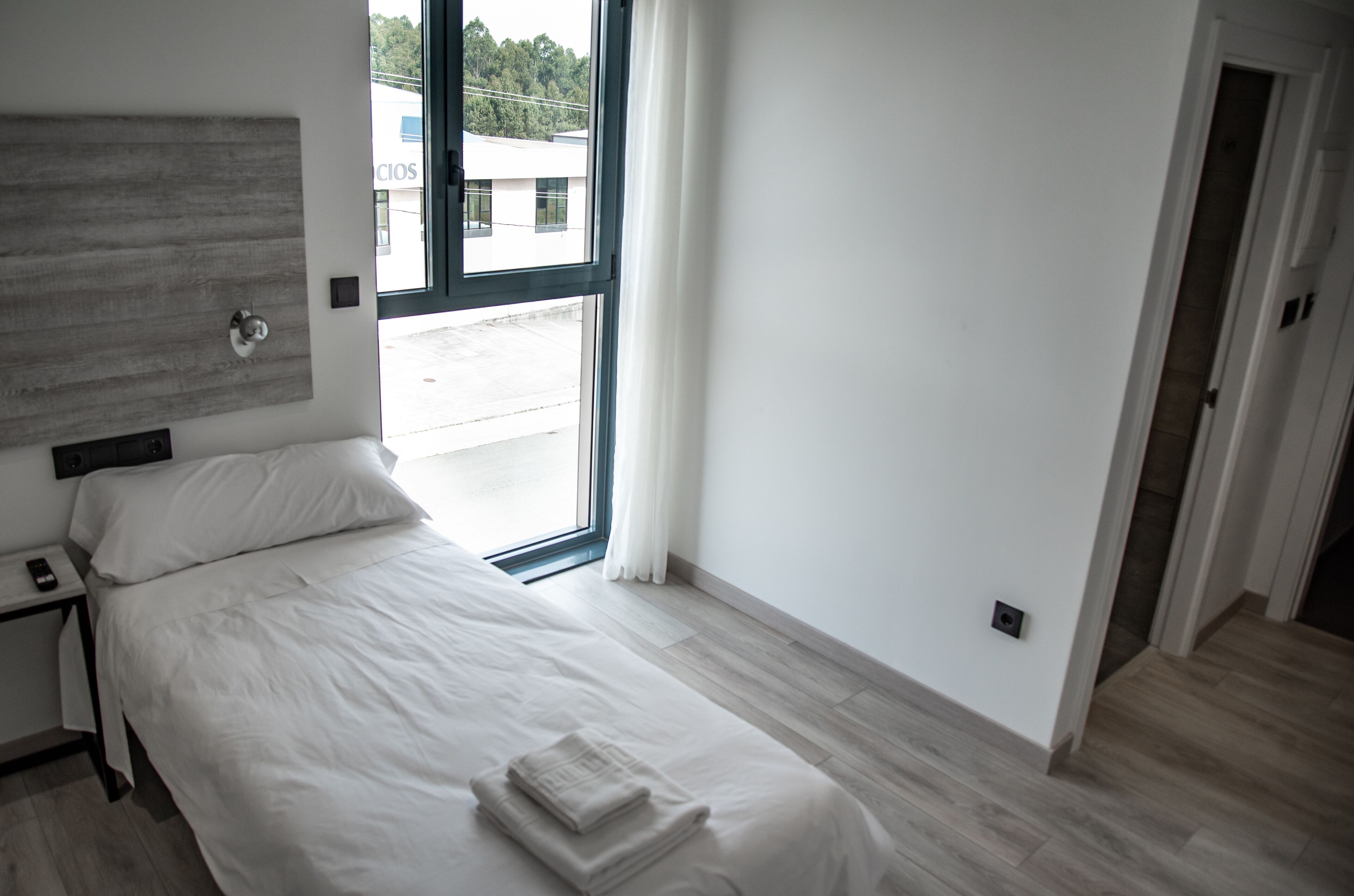 Une chambre à coucher moderne avec une grande fenêtre, un lit recouvert de draps blancs et une tête de lit en bois.