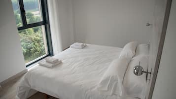 Un dormitorio minimalista con un ventanal grande, una cama bien hecha y una lámpara sencilla de pared.