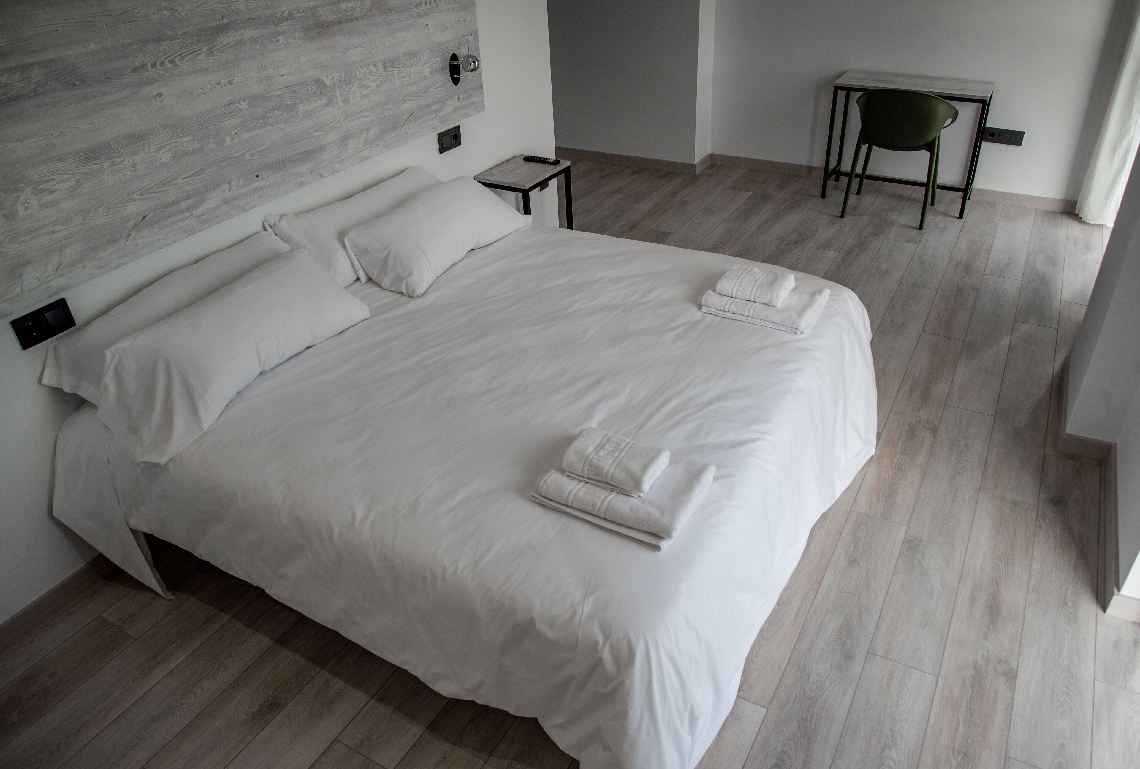 A modern bedroom with a large bed, a bedside table, a chair, and a wooden headboard.