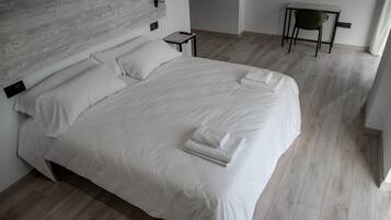 A modern bedroom with a large bed, a bedside table, a chair, and a wooden headboard.