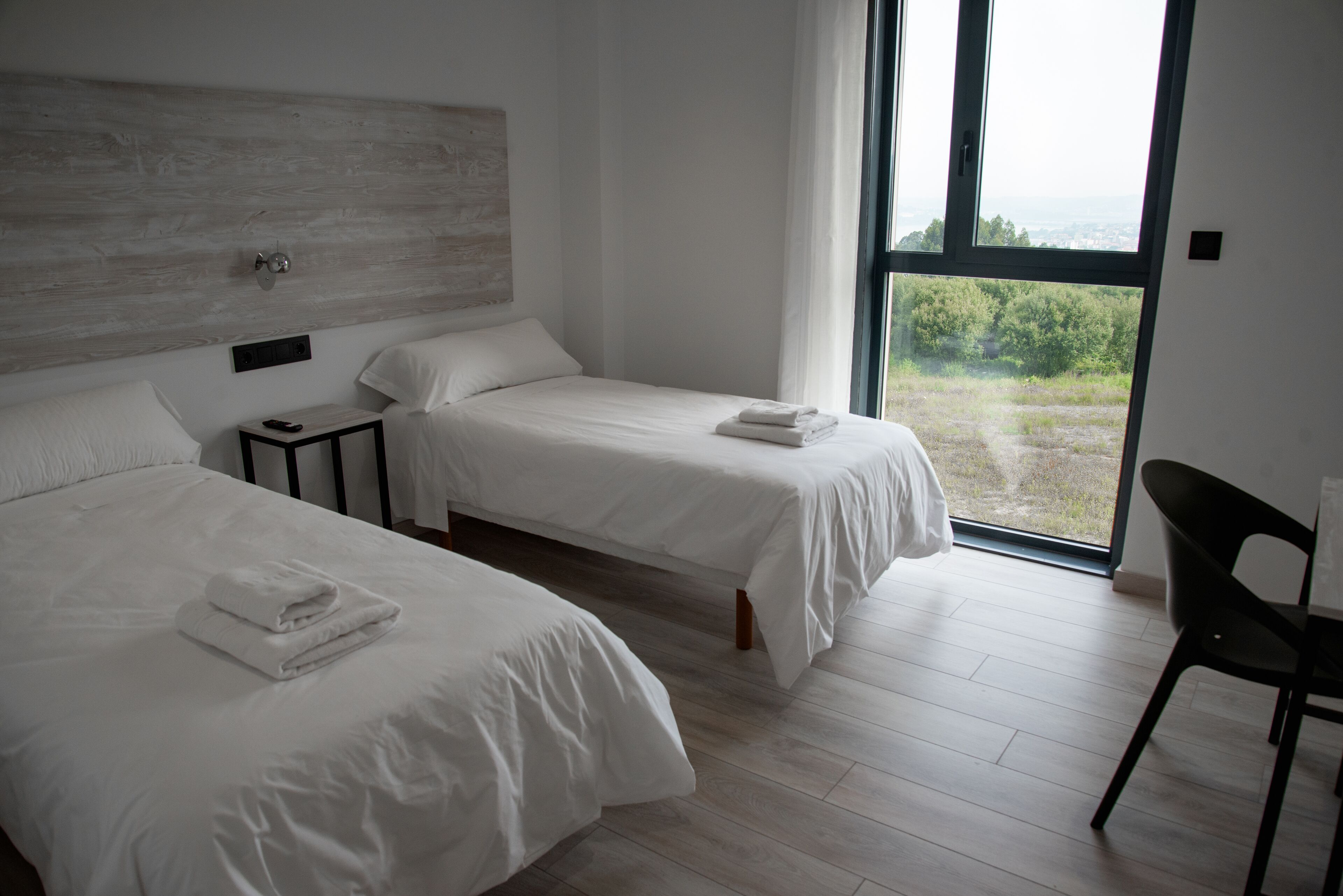 Un dormitorio moderno con dos camas, una mesita de noche y un ventanal que ofrece vistas al exterior.