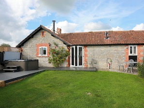 A stone house with a tiled roof, a hot tub, and a patio with outdoor furniture.
