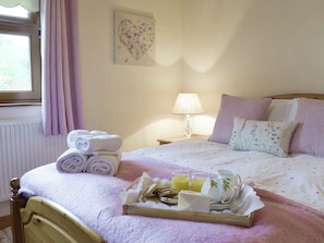 A neatly made bed with a floral-patterned bedspread, a bedside lamp, and a tray with breakfast items.