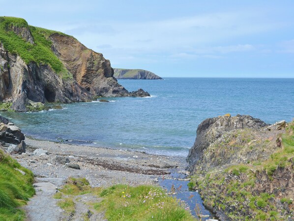 A coastal landscape with rocky cliffs, a pebble beach, and a clear view of the sea.