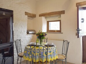 Un coin repas avec une table dressée pour quatre personnes, un vase rempli de fleurs, une fenêtre avec des rideaux et un radiateur.