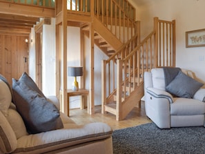 A wooden staircase leading to an upper level, a sofa with cushions, a lamp on a small table, and a framed picture on the wall.