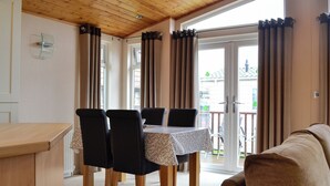 Un comedor con una mesa y sillas, techo de madera y vista a un balcón exterior por una puerta de vidrio.