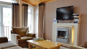 Una sala de estar con un sofá, sillones, una mesa de centro, una chimenea y un televisor montado en la pared.