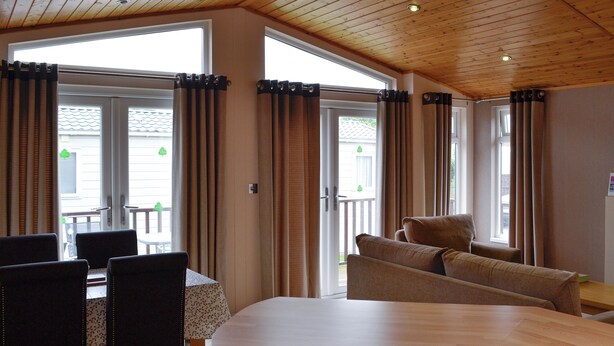 Una habitación con techo de madera, una mesa de comedor con sillas, un sofá y ventanas grandes con cortinas.