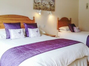 A double bed with a wooden headboard, two pillows, and a purple blanket.