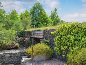 A stone bridge with a metal railing, surrounded by lush greenery and a stone wall.