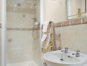 A bathroom with a glass-enclosed shower, a sink with two faucets, and a towel rack with towels.