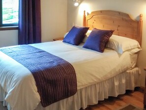 A neatly made bed with a wooden headboard, white bedding, and a brown throw blanket.