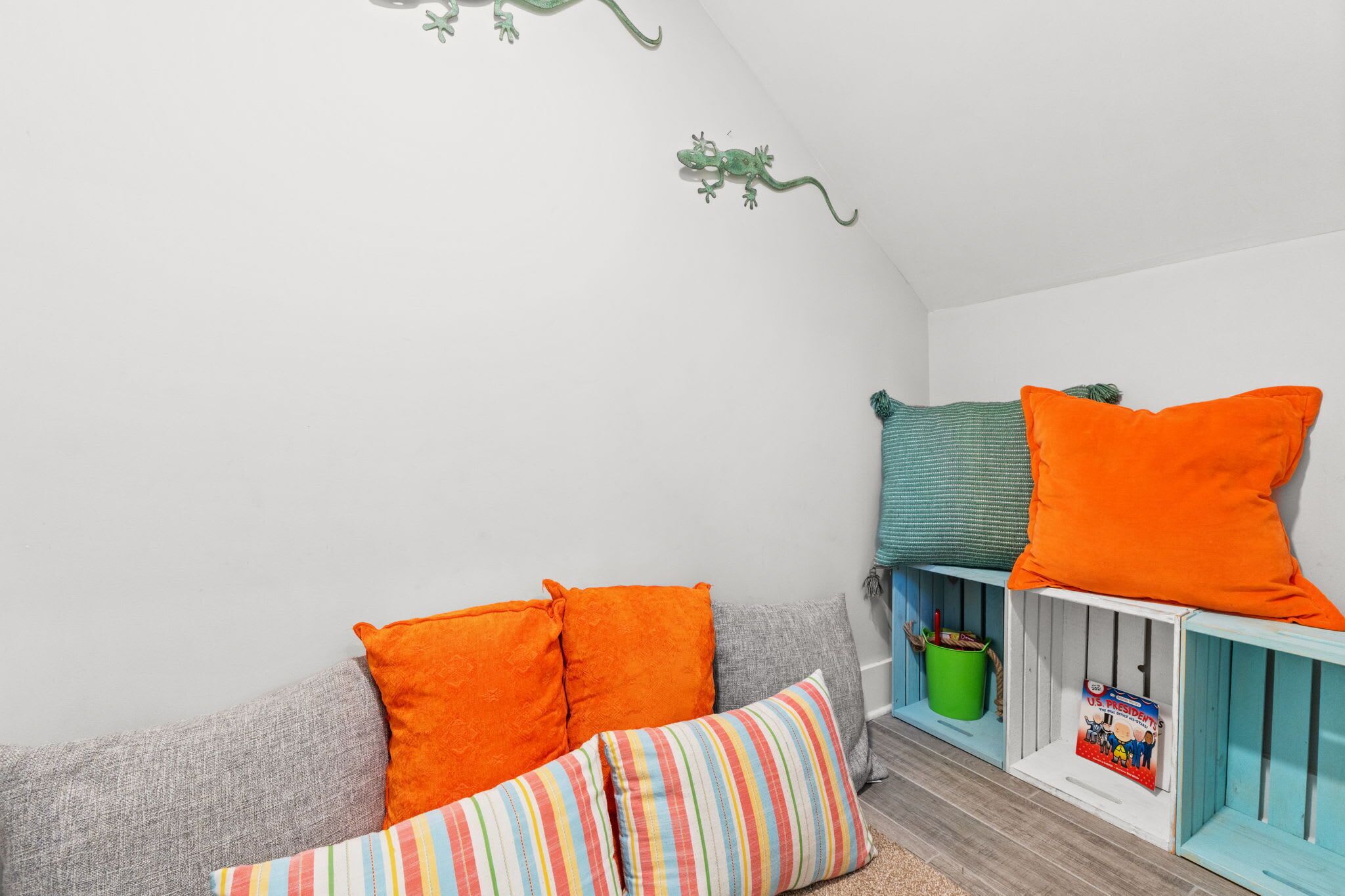 A cozy room with a grey sofa, colorful striped pillows, and a teal and orange pillow on a white shelf.