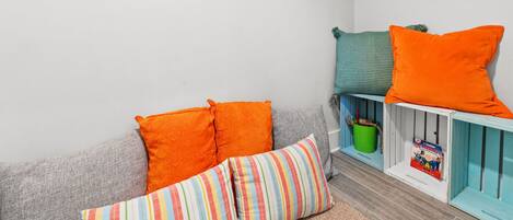A cozy room with a grey sofa, colorful striped pillows, and a teal and orange pillow on a white shelf.