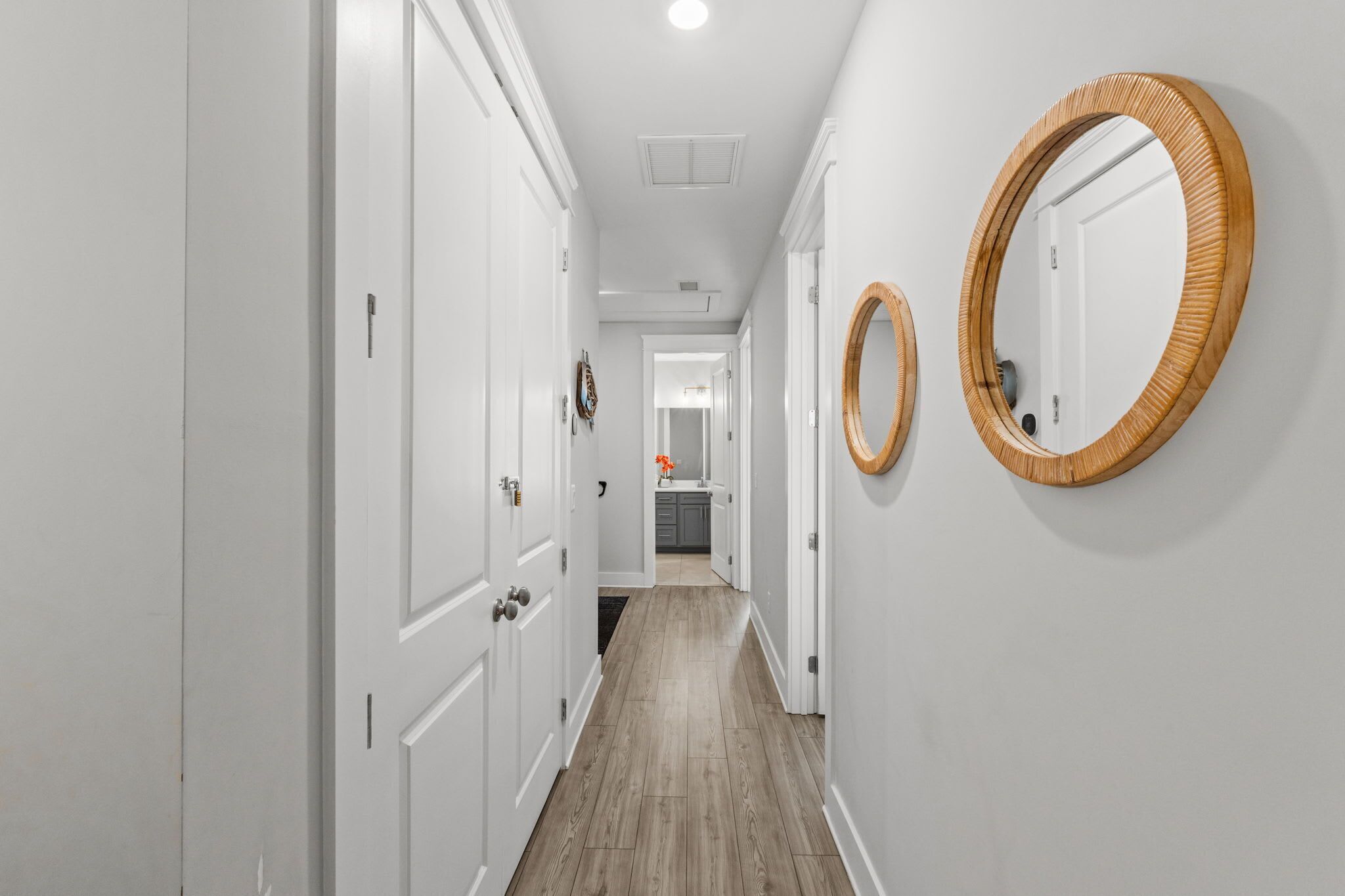 Un couloir avec des portes blanches, un plancher en bois et deux miroirs fixés au mur.