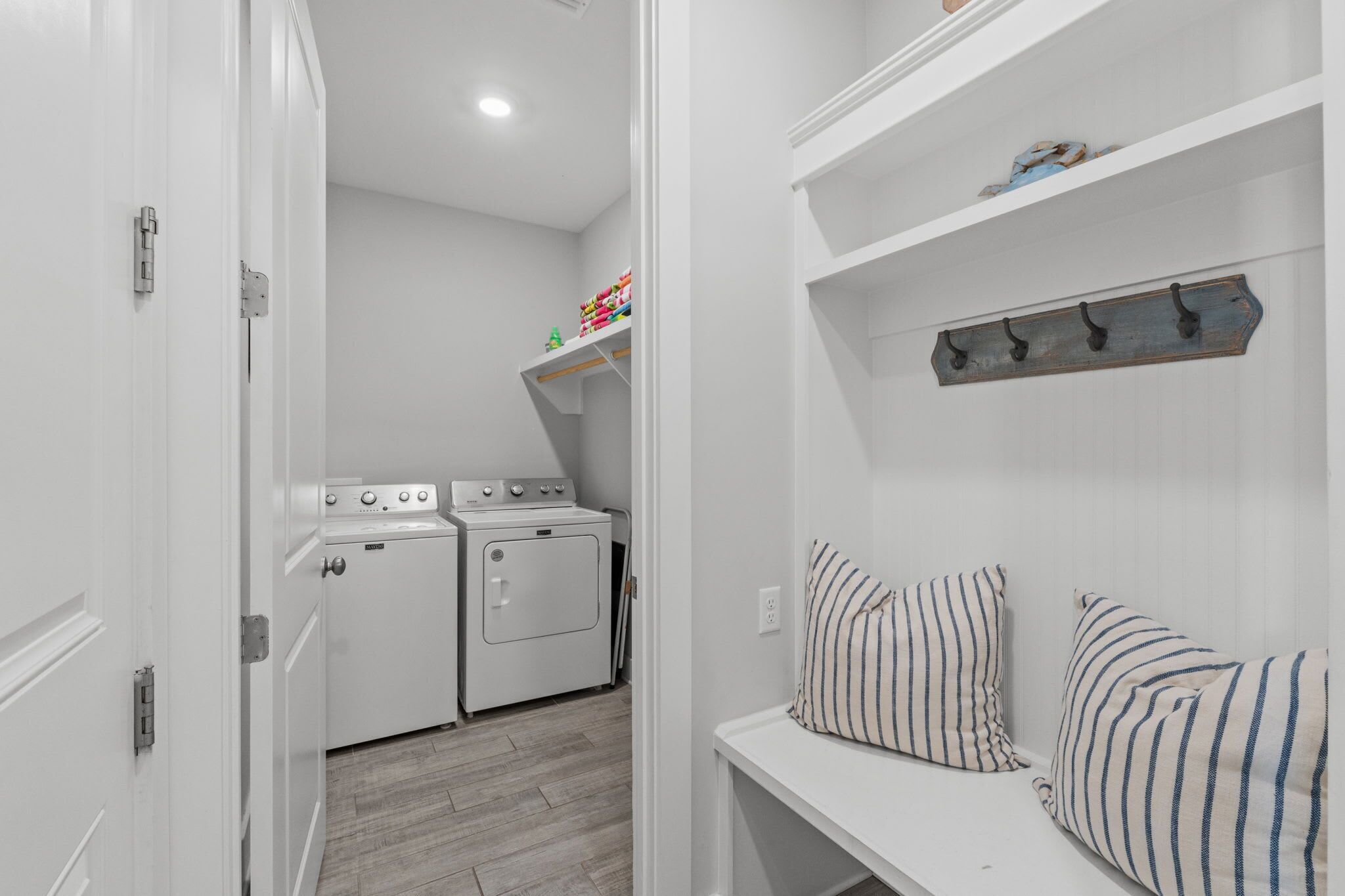 A laundry area with a washer and dryer, a shelf with toys, and striped pillows on a bench.