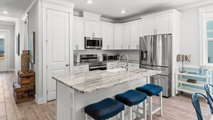 Una cocina moderna con gabinetes blancos, electrodomésticos de acero inoxidable, una isla de mármol con taburetes y un ventanal con vistas.