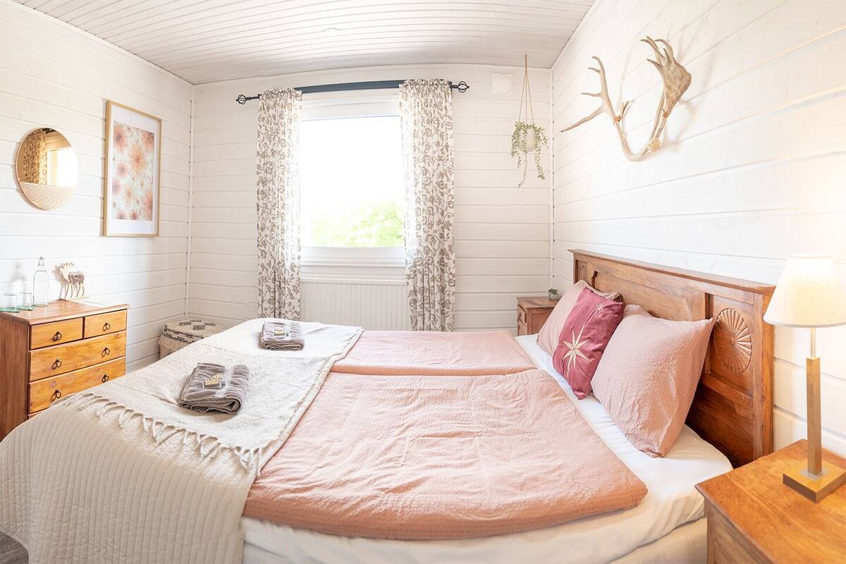 Ein gemütliches Schlafzimmer mit einem Doppelbett, zwei Nachttischen, einer Kommode, einem Fenster mit Vorhängen und Wanddekoration.