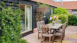 Un patio con una mesa, sillas, un ventanal y un muro de ladrillo.