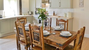 Una mesa de comedor lista para desayuno, almuerzo y cena, con sillas de madera y un jarrón de flores.