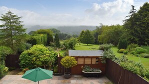 Un jardín con una estructura de madera, un paraguas verde y vistas al campo.