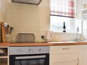 Une cuisine avec un grille-pain, une bouilloire et une bouteille de vin posée sur le rebord de la fenêtre.