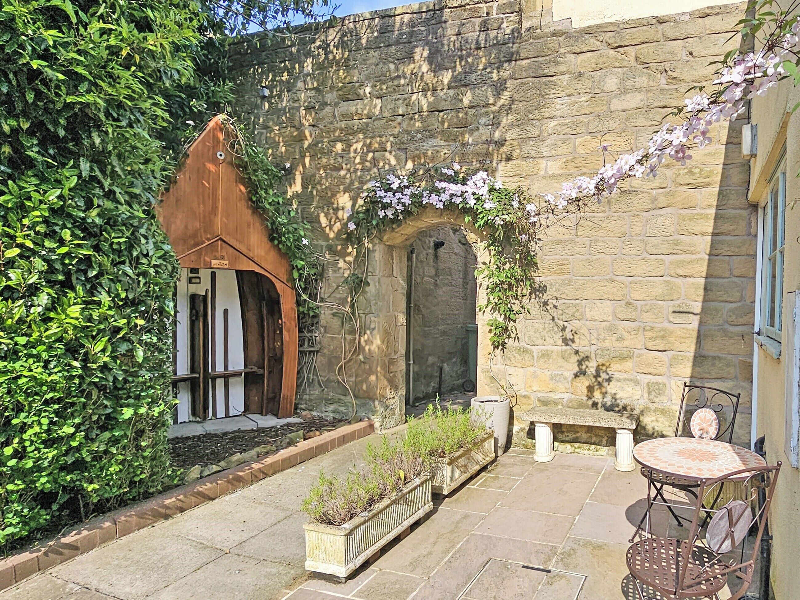 A courtyard with stone walls, a wooden door, a bench, and a table with chairs.