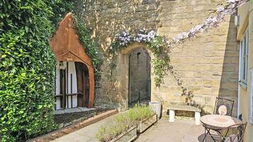 A courtyard with stone walls, a wooden door, a bench, and a table with chairs.
