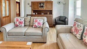 A living room with two sofas, a wooden cabinet, and a red rug. - Converted barn set on a working farm with plenty of walks from the door. (Abererch, near Pwllheli)