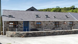 A stone building with a blue door, multiple windows, and a sloped roof. - Converted barn set on a working farm with plenty of walks from the door. (Abererch, near Pwllheli)