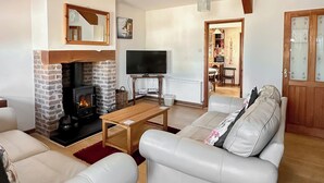 A living room with a fireplace, a television, a sofa, and a dining area. - Converted barn set on a working farm with plenty of walks from the door. (Abererch, near Pwllheli)