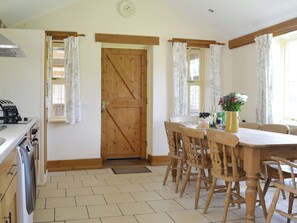 A kitchen with a wooden door, a dining table with chairs, a stove, and a clock on the wall.